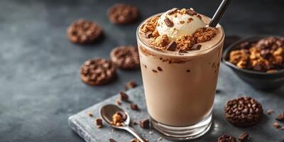 Creamy dessert drink topped with cookie crumbles and ice cream served in a glass on a dark countertop with cookies nearby photo