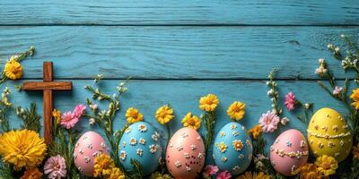 Colorful decorated Easter eggs with flowers and a wooden cross arranged on a blue wooden table photo