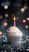 Birthday cupcake with candle shining brightly amid sparkling background photo