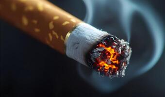 Close-up of a lit cigarette with glowing tip and swirling smoke against a dark background photo