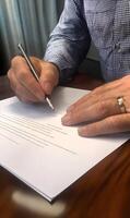 Close up capture of hand signing a document with a sleek pen on a wooden table photo