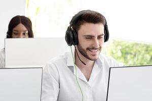 Multinational customer service representatives in headsets working behind their PC monitors at call centre. Group of hotline operators communicating with clients, promoting products or making poll photo
