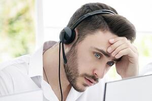 Irritated hotline operator dealing with client's complaint at call centre. Young technical support consultant having problem solving customer's request at modern open space office photo