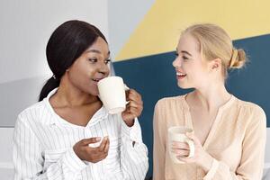 Female tech support operators having coffee and friendly chat during their break at open space office, free space. Helpdesk agents talking and enjoying each other's company at call centre photo