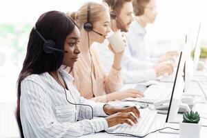 Line of call centre employees with headphones working on computers at open space office photo