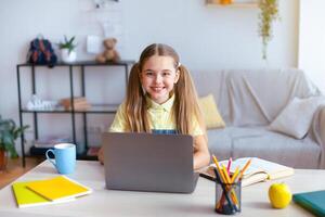 Distance Education. Smiling girl sitting at table, using laptop computer and looking at camera, watching tutorial, virtual lecture or lesson, studying online at home. E-learning And Knowledge photo