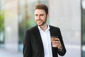 Handsome business manager with takeout coffee and tablet computer near his office building at big city photo