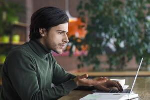 Young man freelancer having problem with project, looking at laptop screen, working at cafe, empty space photo