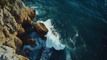 Dramatic aerial view of ocean waves crashing against rocky cliffs along the coastline photo