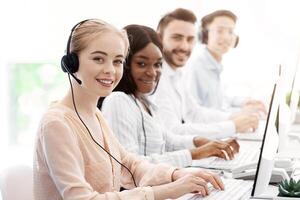 Group of call centre employees smiling and working on computers at light office, space for text photo