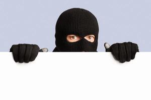 Closeup portrait of disguised looter peeping out white blank advert billboard, isolated over white studio background photo