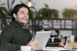 Dreamy male freelancer working on new project at cafe, using digital tablet, copy space photo