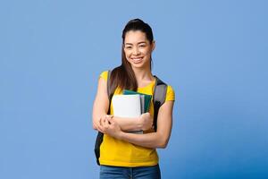 Portraif of smiling asian student girl with backpack and workbooks posing over purple studio background, looking at camera, copy space photo