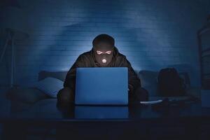 Private Information Security Concept. Masked hacker using pc, sitting in the dark on couch, stealing big data photo