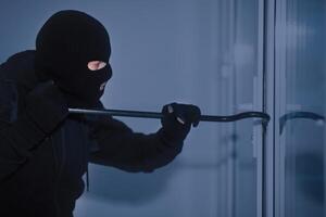 Home Security Concept. Burglar in Action Trying To Break Into the House Using Crowbar, Side View photo