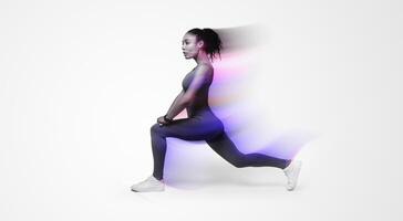 Young African American woman in activewear performing forward lunges on pink studio backdrop, displaying fitness routine, making stretching legs exercise looking aside, side view shot photo