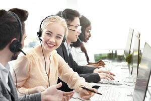 Smiling customer support workers communicating to solve client's problem together at call centre office. Positive hotline operators with headsets having conversation at workplace photo