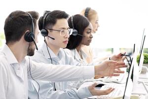 Customer support service concept. Helpline operator consulting his colleague at call centre. Technical support agents talking to each other, solving client's inquiry at open space office photo
