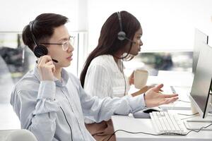 Frustrated Asian helpdesk operator dealing with client's problem at modern call centre. Technical support agent consulting customer online, providing telecommunications services photo