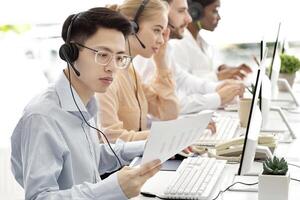 Asian hotline operator working with documents, providing technical support services to clients, free space. Call centre representatives talking to customers or selling goods online photo