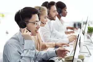 Telecommunications concept. Positive hotline consultants selling goods or services at call centre, copy space. Diverse team of tech support managers dealing with customers' needs at modern office photo
