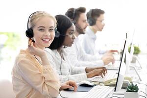 Team of diverse hotline operators with headphones providing service to clients at call center. Young customer support representatives working in telemarketing or telecommunications at modern office photo