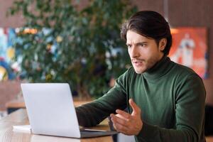 Angry man looking at laptop screen, having troubles with job, working at cafe, empty space photo