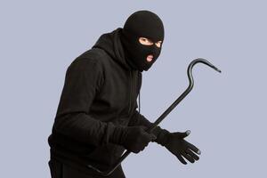 Cat Burglar Concept. Portrait of sneaky masked criminal holding crowbar, copy space, isolated over white studio wall photo