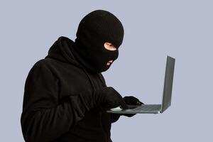 Computer Hacker. Masked criminal wearing black balaclava downloading private information, isolated on white wall photo