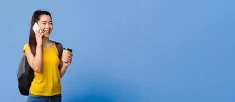 Cheerful Asian Female College Student With Backpack Talking On Cellphone And Drinking Coffee, Standing Over Purple Background In Studio, Having Break In Study, Enjoying Mobile Conversation, Copy Space photo