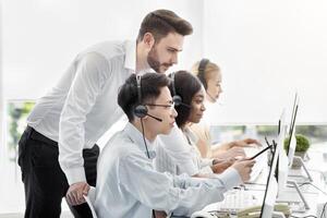 Customer service administrator helping his supervisee to execute client's request at call centre. Hotline colleagues working at problem together in contemporary open space office photo