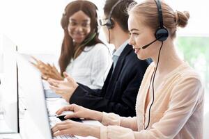 Team of call center operators in headsets talking with customers at open space office photo