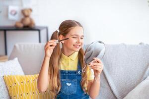 Young Girl Doing Makeup, Applying Black Mascara on Eyelashes with Brush, Holding And Looking At Mirror photo