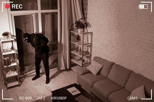 Surveillance Concept. Thief With Crowbar Wearing Balaclava Entering House, Scene Through CCTV Camera, High Angle View photo