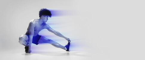 Fitness workout. Young shirtless athletic man exercising in extended leg squat pose, stretching legs and touching toes, demonstrating flexibility and strength over gray studio background photo