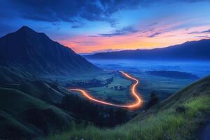 Winding road illuminated by lights at twilight in mountain valley photo
