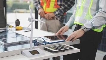 Two men working on a table with solar panels and wind turbines video