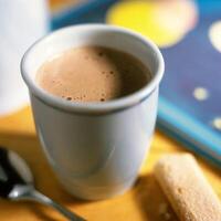 A cup of hot chocolate with a spoon and a book photo