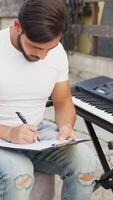 Man Is Composing A Music Writing On The Sheet Music And Rehearsing On Keyboard video