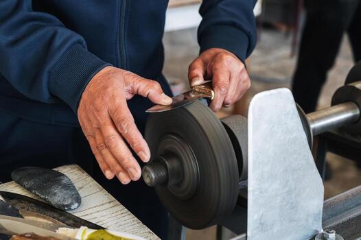grinder sharpens the knife by holding it in hands on abrasive rotating wheel of the sharpening machine in workshop photo