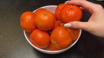 bright oranges tangerines stand in a white plate on a black table a hand picks up and puts oranges in a plate fruits video