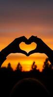 Silhouette of two hands making a heart shape with the sun setting in the background photo