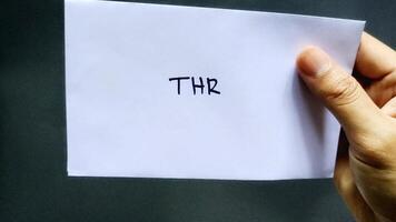 This man holding a white envelope that says THR. This envelope contains one month's salary allowance which is usually given to employees before the Islamic holidays photo