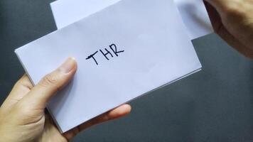 Close up of a man's hand holding several envelopes with THR written on them. These envelopes containing holiday allowances are usually given to family and relatives before Eid al-Fitr photo