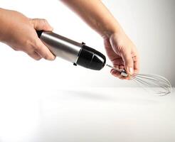 Modern immersion blender with whisk in hand on white background, close-up photo