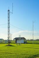 Weather monitoring station with tower and shelter in open field under clear sky photo