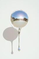 Reflective glass sphere with droplet, casting a shadow against a light background. photo