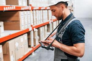Checking data in the tablet. Employee in uniform is working in the storage at daytime photo