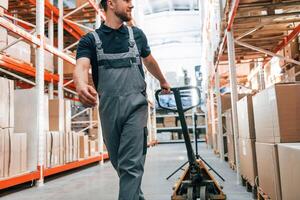 Walking with platform trolley. Employee in uniform is working in the storage at daytime photo