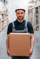 With delivery package in hands. Employee in uniform is working in the storage at daytime photo
